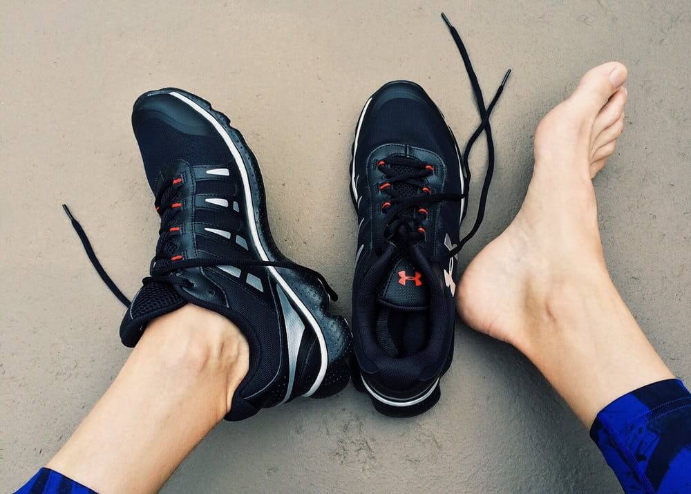 Picture of someone's black shoes, one shoe is one and a barefeet next to the sneakers