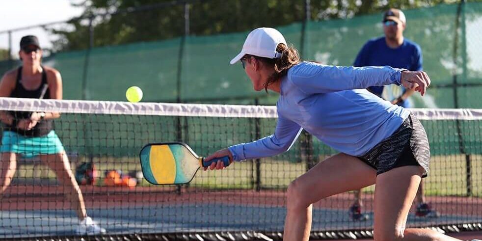A woman hits a dink shot while playing pickleball.