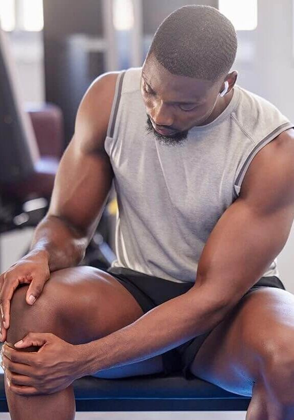 Man, fitness and knee injury in gym after workout, training or intense exercise. Earphones, health and bodybuilder male from Nigeria suffering from sore leg, muscle pain or joint inflammation.